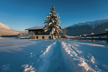 Deep snow trail path to former film location of the 'Bergdoktor' in sunlit alpine winter landscape in Wildermieming, Tirol, Austria