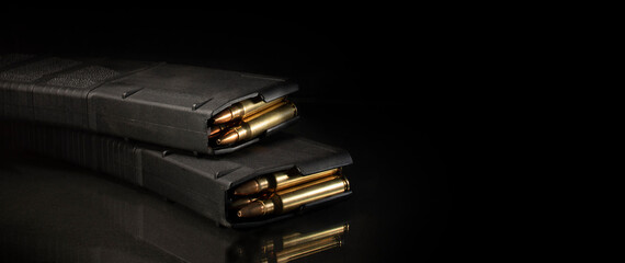 Two loaded AR-15 magazines on a black background with a reflection and room for copy