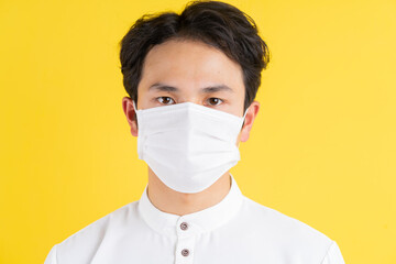 Young man wearing a mask standing and looking at the camera on a yellow background