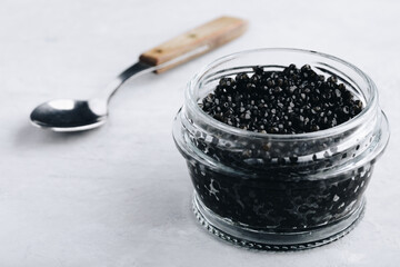 Fototapeta na wymiar Black caviar in glass jar on white stone background, luxurious delicacy appetizer.