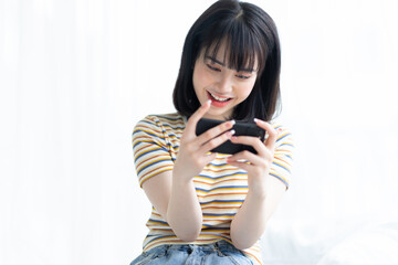 Beautiful Asian woman playing game on smart phone in bedroom