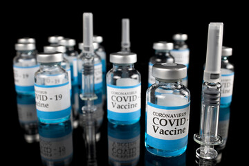 Fighting covid-19: Glass vials labelled with COVID-19 text and glass disposable syringes on black background.