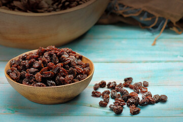 Dried raisins in wooden bowl over wooden table.