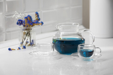 A cup of blue Thai tea against  glassware teapot and empty glass mug on the kitchen table. Detox tea concept.