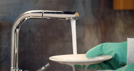Close up of person in gloves washing dishes with sponge and foam in kitchen sink