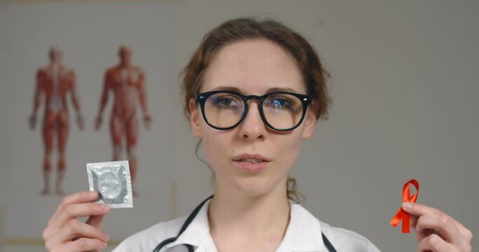 Female doctor holding condom and red ribbon warning against aids
