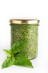 Pesto sauce in a glass jar isolated with fresh basil leaves on white background. Traditional homemade Italian sauce pesto and basil leaves