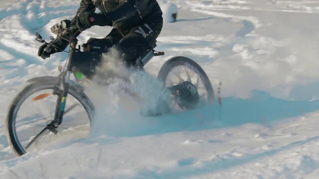 Cyclist in Black Clothes, Helmet and Snow Glasses Riding on Electric Bike in the Snow in Winter Forest. E-Bike Riding and Drifting at Cold Sunny Day - Slow Motion