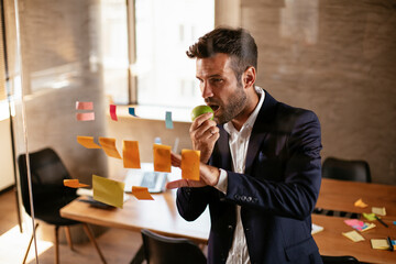 Businessman in conference room use sticky notes on glass wall. Handsome businessman making a business plan