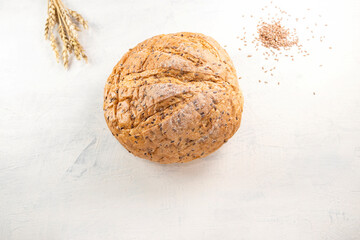 Fresh, tasty, round wheat bread with flax seeds next to wheat ears on white table with place for text. Copy space.