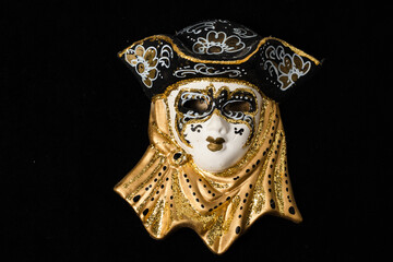 Venetian masks of white and black ceramic ornament with golden or gold highlights. Black background.