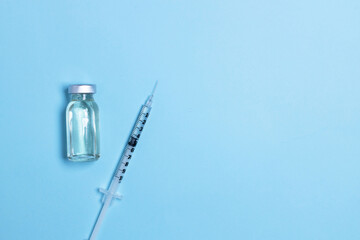 Syringe with medicine from glass vial on light blue background, flat lay. Vaccination against...