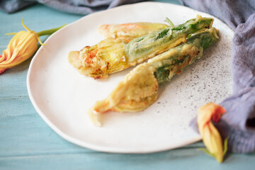 Battered and fried Courgette or Zucchini squash blossoms shot from above over a blue rustic table.