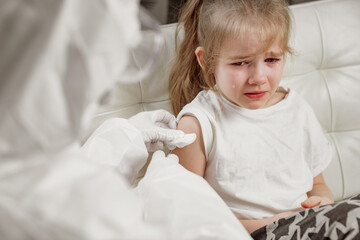 Fototapeta premium Little girl cries her hurt and scared. injection during illness. Vaccination. call the doctor at home. Pandemic.