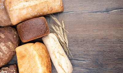 Various types of loaves of wheat and rye bread on a wooden table with place for text.