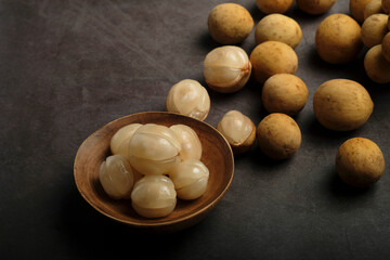 Longkong, tropical fruit in a wooden bowl on dark background.