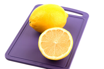 A whole lemon and half a fruit on a plastic cutting board over a white background.