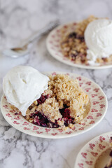 Blackberry and Blueberry Cobbler topped with a golden oatmeal crisp with ice cream. Extreme selective focus with blurred background.