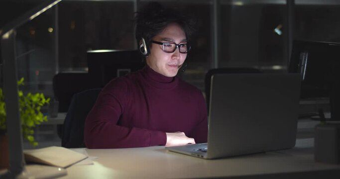 Asian businessman in headset working with computer late at night in client support service