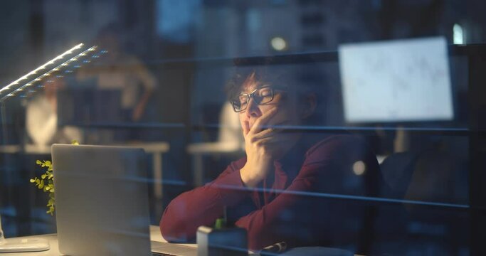 Korean businessman yawning sitting at computer working late at night office