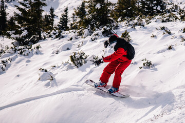 A guy in a red jumpsuit eating freeride on a snowboard on a snowy slope