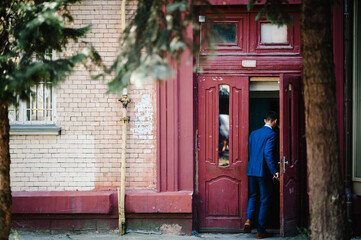 Man open the door and enters the home. Old wood red door with damaged brick wall. Ancient building with rusted door. Facade house. Back view.