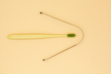 metal scraper or tongue cleaning brush and a toothbrush on beige background. Hygiene of the oral cavity