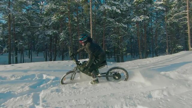 Cyclist in Black Clothes, Helmet and Snow Glasses Riding on Electric Bike in the Snow in Winter Forest. E-Bike Riding and Drifting at Cold Sunny Day - Super Slow Motion