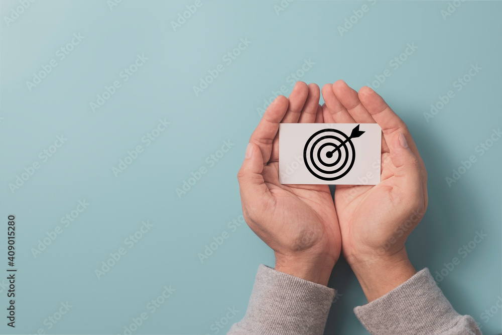 Poster hand holding white paper which print screen dartboard with arrow on blue background and copy space, 