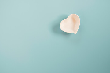 Fototapeta premium White small ceramic heart shape bowl on blue and copy space on blue background for valentines’s day concept.
