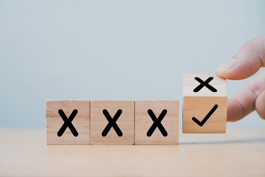 Hand flipping wooden cube block to change cross incorrect to correct mark.
