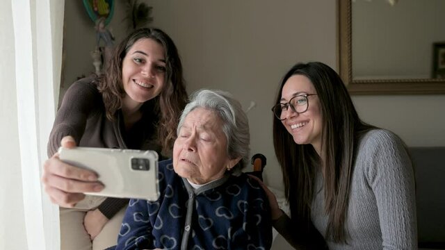 Granddaughters with grandmother having a video call. Old woman in wheelchair. 