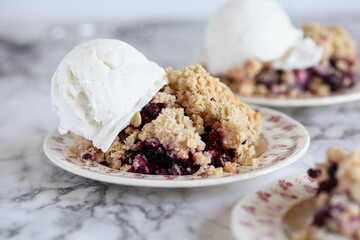 Blackberry and Blueberry Cobbler topped with a golden oatmeal crisp with ice cream. Extreme selective focus with blurred background.