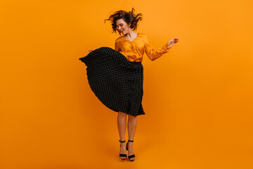 Graceful short-haired girl jumping on yellow background. Studio shot of charming woman in black skirt.