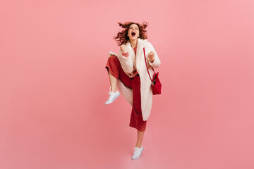 Full length view of lady fooling around on pink background. Studio shot of dancing girl in trendy coat.