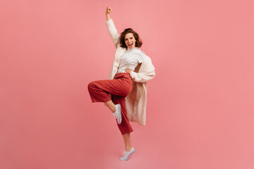 Full length view of pleased young lady in coat. Studio shot of positive girl fooling around on pink...