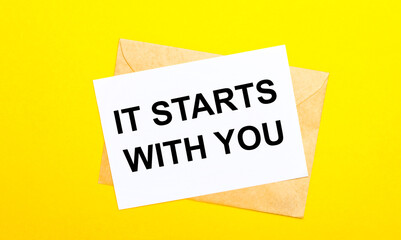 On a yellow background, an envelope and a card with the text IT STARTS WITH YOU. View from above