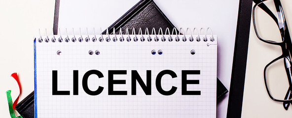 The word LICENCE is written in red in a white notebook next to black-framed glasses.