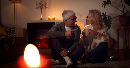 Happy senior couple relaxing together near fireplace and drinking coffee at home