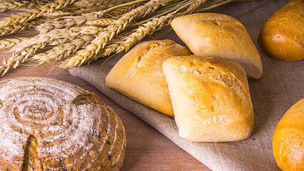 Freshly baked homemade bread and buns on a wooden table with dry wheat ears - rustic style
