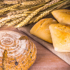 Freshly baked homemade bread and buns on a wooden table with dry wheat ears - rustic style