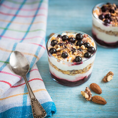 Dessert with yogurt granola and currant berries in glass glasses on a blue wooden background with a spoon and a napkin