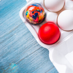 Painted for easter and simple eggs in a white container on a wooden blue background, top view - holiday concept