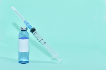 Medical ampoule (vial) with vaccine and syringe on light blue background. White label on bottle, space for text. vaccination against covid-19, flu. Cosmetological injections. COVID-19 vaccine vial