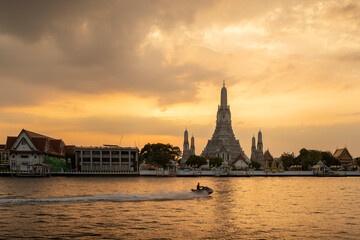 Wat Arun or temple of dawn is a landmark of bangkok,Thailand. The famous and beautiful architecture pagoda located near Chaopraya river. A man travel by jet ski at sunset to destination.