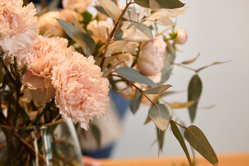 Florist works with colors. Flower seller chooses flowers for future bouquet. Flowers shop worker in a mask standing in flower shop and checking flowers in glass vase.