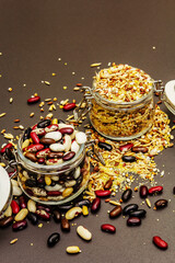 Mix of variety of cereals and beans in glass jars on black stone background