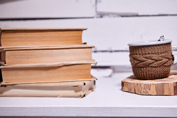 Pile of books with cup on wooden table.