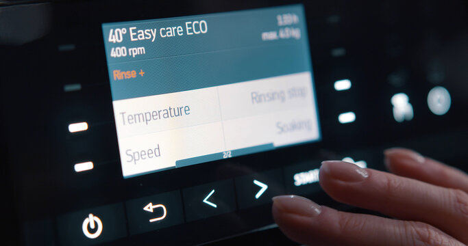 Close Up Of Woman Selecting Regime And Temperature On Washing Machine Control Panel