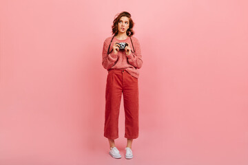 Full length view of sad woman with vintage camera. Studio shot of female photographer standing on pink background.